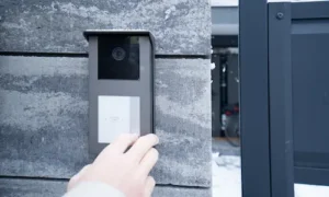 Hand using a wall-mounted video doorbell and access control system at a property entrance.