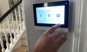 Hand operating a wall-mounted touchscreen home security and smart home control panel.